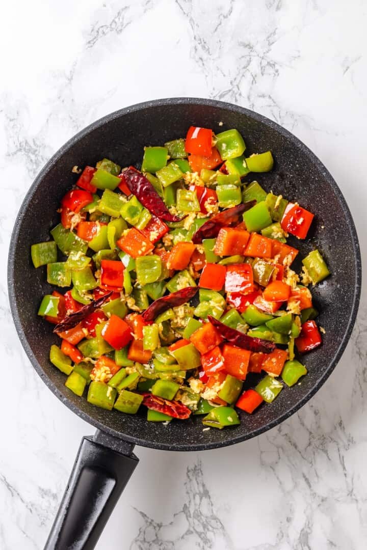 This crispy kung pao tofu is made with bell peppers, crunchy peanuts and a sweet-spicy sauce for a dinner that's even better than takeout! Bell peppers cooking in skillet with chili peppers.