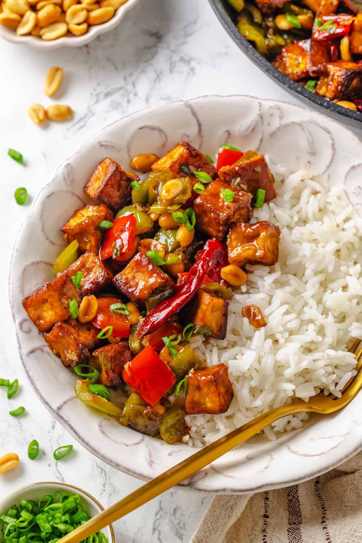 This crispy kung pao tofu is made with bell peppers, crunchy peanuts and a sweet-spicy sauce for a dinner that's even better than takeout! Bowl of white rice and kung pao tofu with fork.