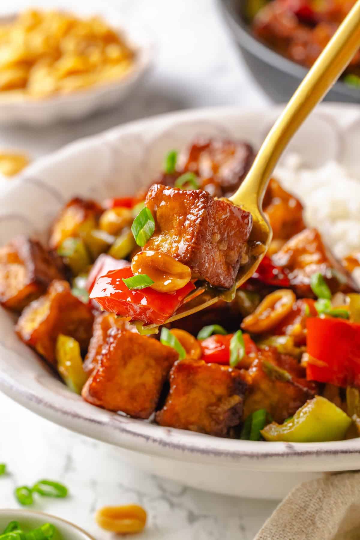 This crispy kung pao tofu is made with bell peppers, crunchy peanuts and a sweet-spicy sauce for a dinner that's even better than takeout! Forkful of kung pao tofu held over bowl.