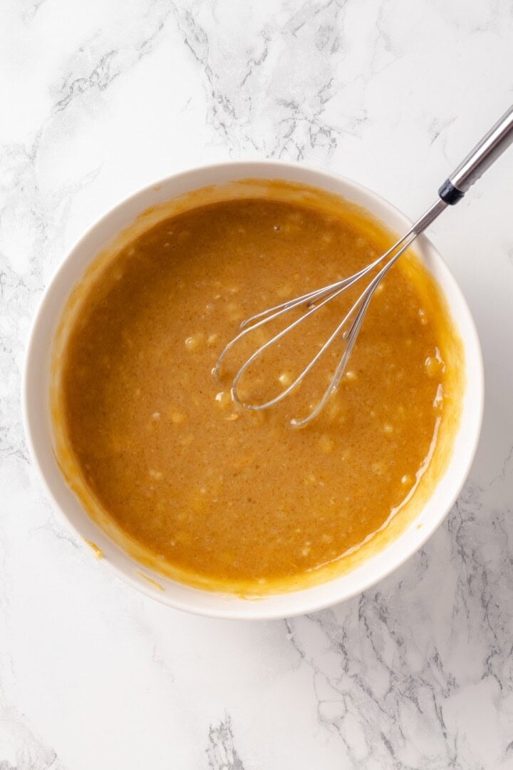 These moist peanut butter banana muffins are made with whole wheat flour and chocolate chips for a wholesome muffin that tastes like a treat! Wet ingredients for peanut butter banana muffins in bowl with whisk.