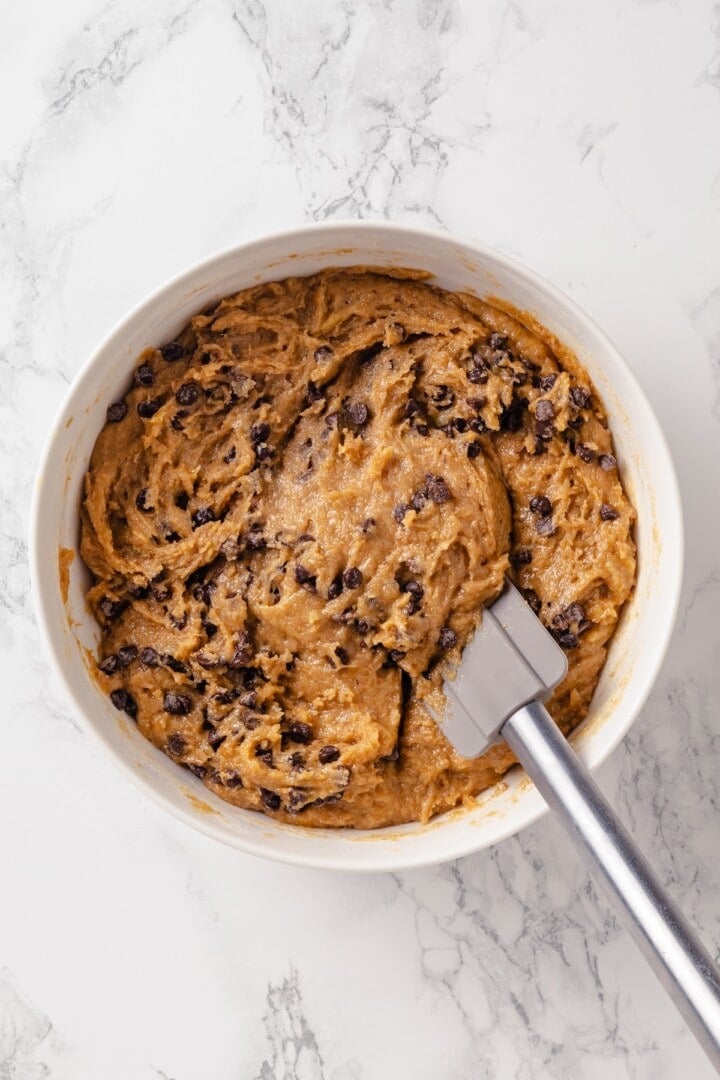 These moist peanut butter banana muffins are made with whole wheat flour and chocolate chips for a wholesome muffin that tastes like a treat! Batter for peanut butter banana muffins in bowl with rubber spatula.