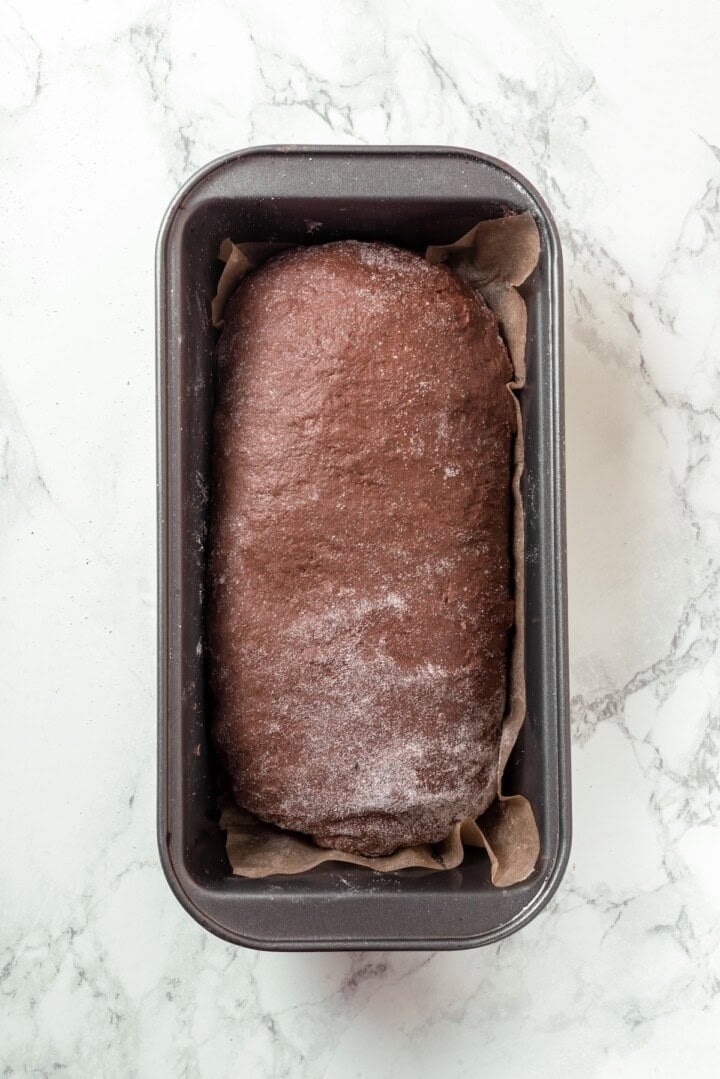 This no-knead dark pumpernickel bread has rich rye flavour and cocoa undertones, perfect for sandwiches and toast. It's so easy to make too! Baked loaf of pumpernickel bread in pan.