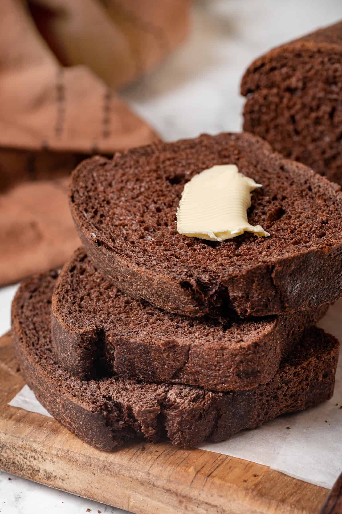 This no-knead dark pumpernickel bread has rich rye flavour and cocoa undertones, perfect for sandwiches and toast. It's so easy to make too! 3 slices of pumpernickel bread, with butter on top slice.