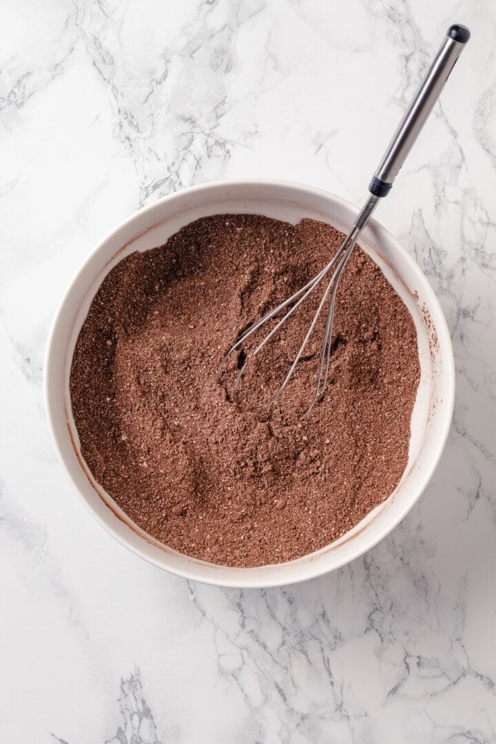 These fudgy vegan sweet potato brownies are made with maple syrup and cocoa for a treat that’s naturally sweet, gluten-free, and oh so rich! Dry ingredients for brownies in bowl with whisk.