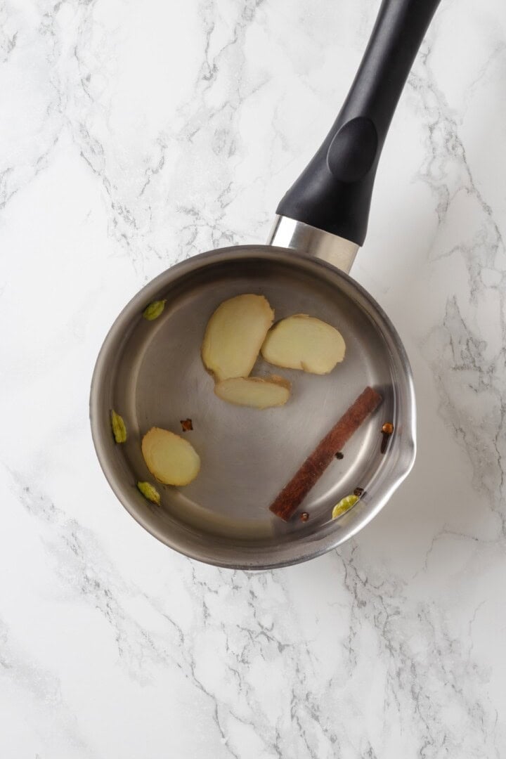 This cozy vegan spiced chai chai is creamy, warmly spiced, and easy to make at home with oat milk and whole spices. Spices in pot of water.