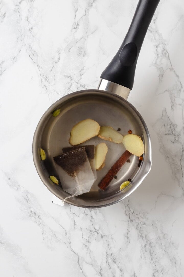 This cozy vegan spiced chai chai is creamy, warmly spiced, and easy to make at home with oat milk and whole spices. Spices and tea bags in pot of water.