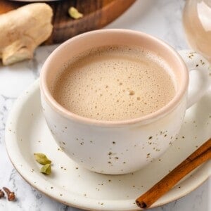 Spiced chai in mug on saucer with cinnamon stick.