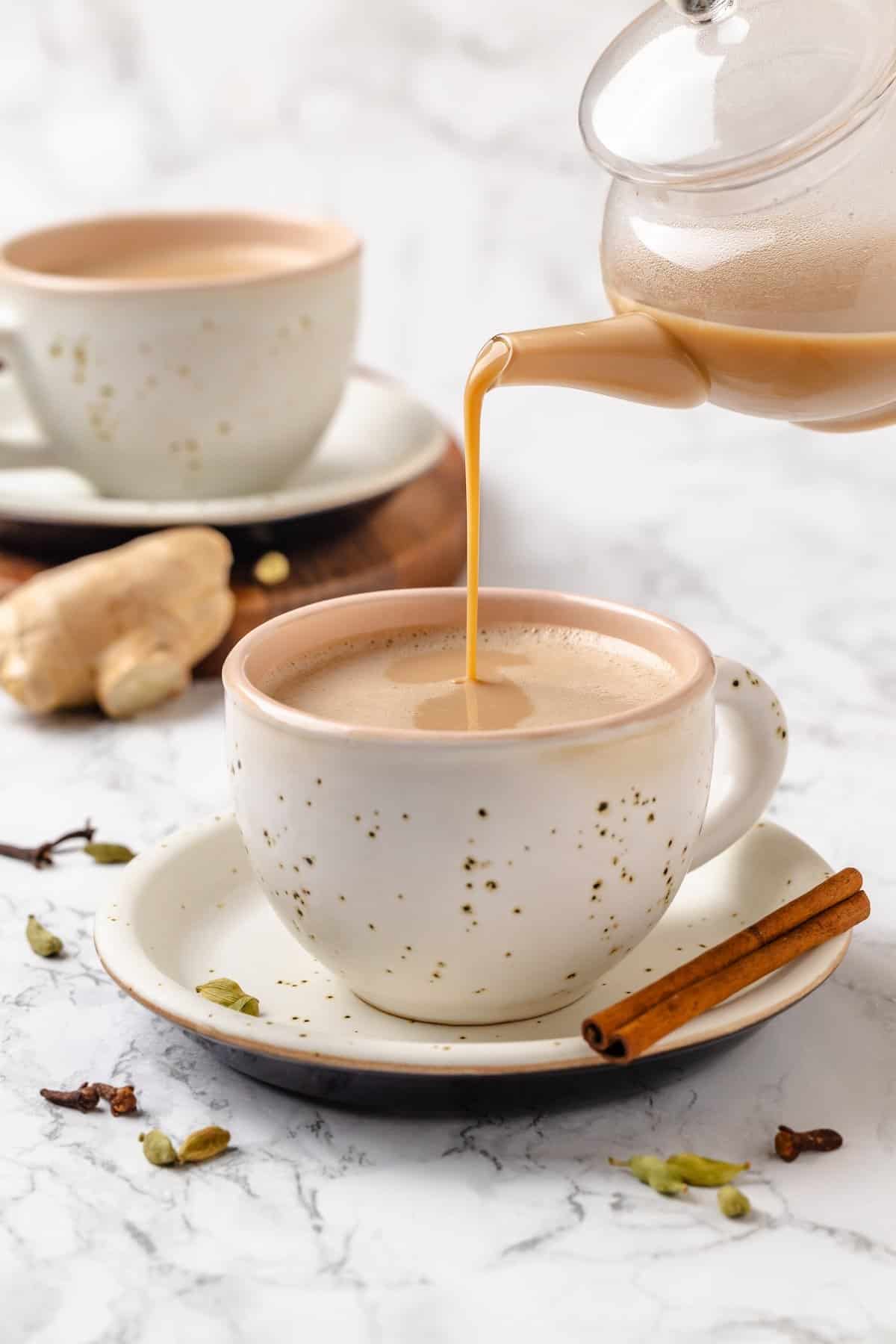 This cozy vegan spiced chai chai is creamy, warmly spiced, and easy to make at home with oat milk and whole spices. Pouring spiced chai from teapot into mug.