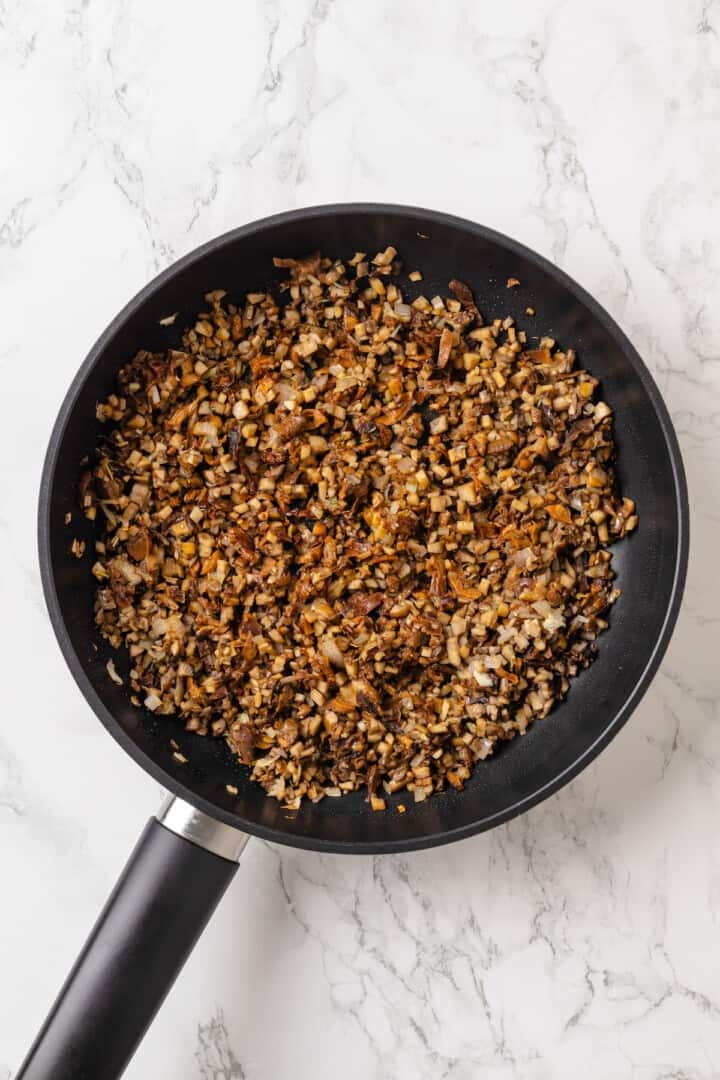 This homemade mushroom ravioli is filled with porcini, cremini and ricotta, then tossed in a creamy vegan Parmesan sauce. Restaurant-worthy! Sauteed mushrooms in skillet.