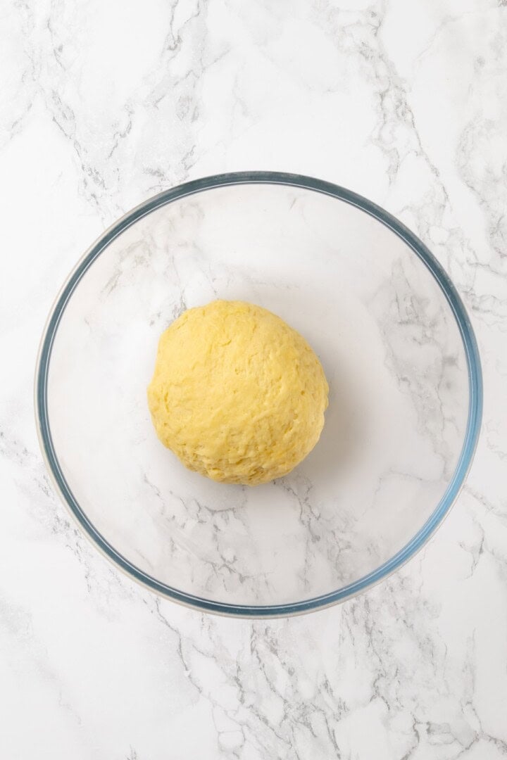 This homemade mushroom ravioli is filled with porcini, cremini and ricotta, then tossed in a creamy vegan Parmesan sauce. Restaurant-worthy! Ball of pasta dough in glass bowl.