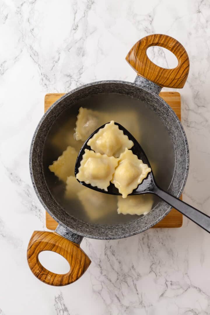 This homemade mushroom ravioli is filled with porcini, cremini and ricotta, then tossed in a creamy vegan Parmesan sauce. Restaurant-worthy! Lifting 3 mushroom ravioli from pot of water.