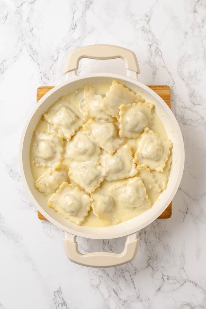This homemade mushroom ravioli is filled with porcini, cremini and ricotta, then tossed in a creamy vegan Parmesan sauce. Restaurant-worthy! Skillet of vegan mushroom ravioli with creamy sauce.