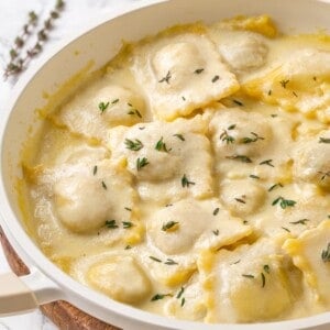 Pan of mushroom ravioli with vegan parmesan sauce and thyme.