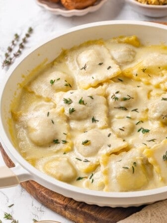 Pan of mushroom ravioli with vegan parmesan sauce and thyme.