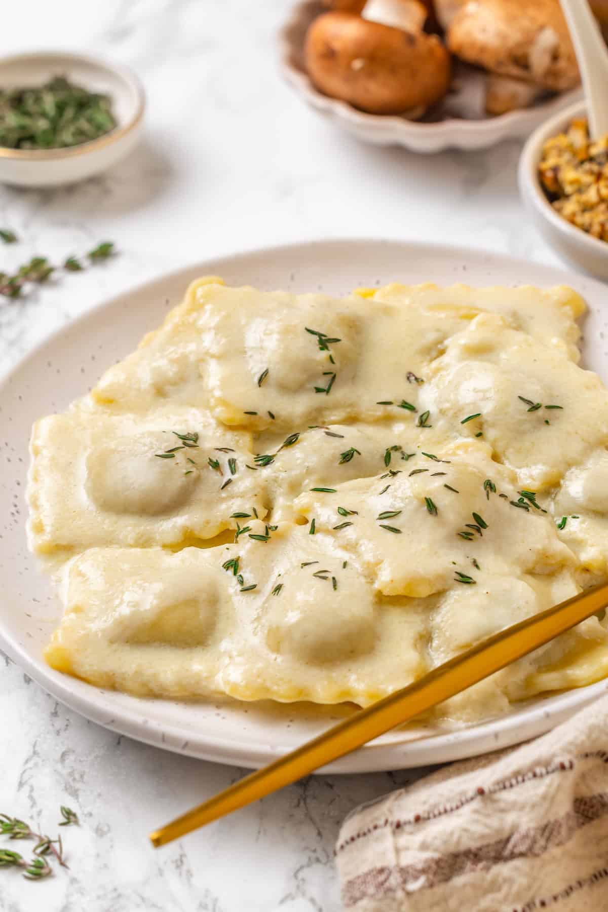 This homemade mushroom ravioli is filled with porcini, cremini and ricotta, then tossed in a creamy vegan Parmesan sauce. Restaurant-worthy! Plate of mushroom ravioli with fresh thyme.