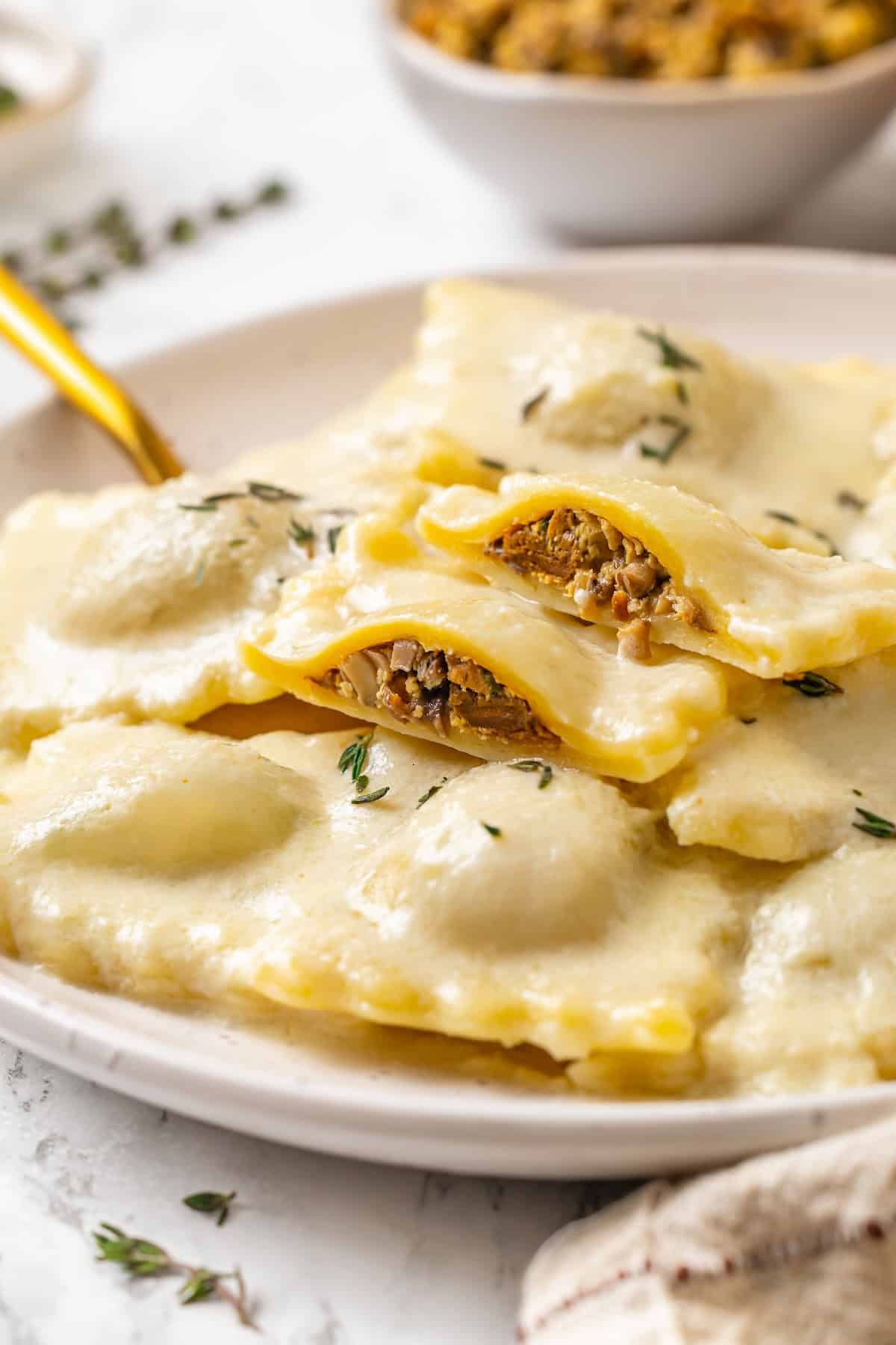 This homemade mushroom ravioli is filled with porcini, cremini and ricotta, then tossed in a creamy vegan Parmesan sauce. Restaurant-worthy! Plate of mushroom ravioli, with two sliced open to show filling.