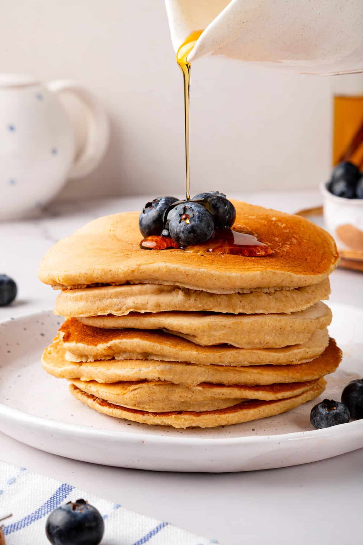 These oat flour pancakes are thick and fluffy, made with simple ingredients and they're naturally gluten-free and vegan. A game changer! Pouring maple syrup onto stack of oat flour pancakes.