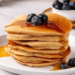 Stack of oat flour pancakes topped with blueberries and syrup.