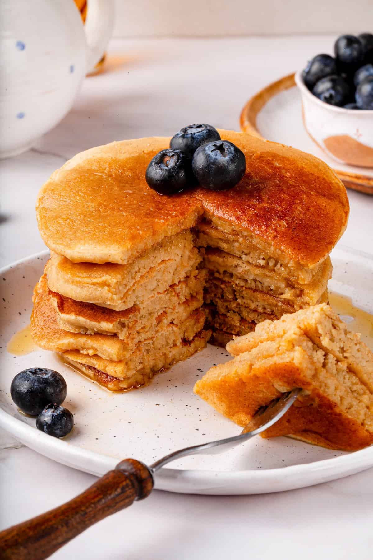These oat flour pancakes are thick and fluffy, made with simple ingredients and they're naturally gluten-free and vegan. A game changer! Stack of oat flour pancakes with wedge cut out to show texture.