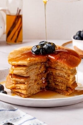 Drizzling maple syrup over stack of oat flour pancakes.