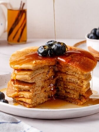 Drizzling maple syrup over stack of oat flour pancakes.