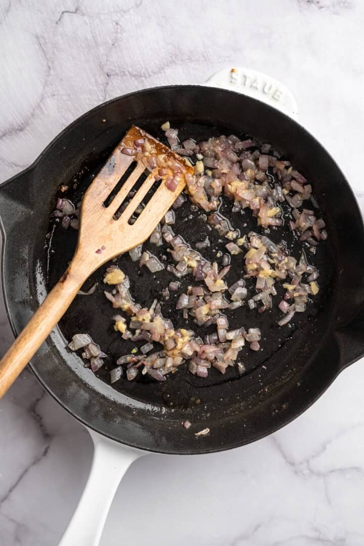 This one pot cheesy tomato gnocchi is creamy, comforting, and ready in under 30 minutes for an easy vegan weeknight dinner! Red onions and garlic cooking in skillet.