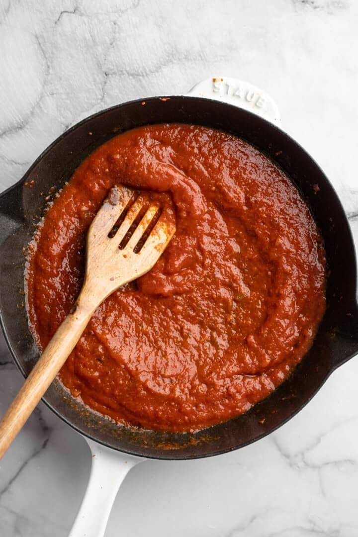 This one pot cheesy tomato gnocchi is creamy, comforting, and ready in under 30 minutes for an easy vegan weeknight dinner! Stirring tomato sauce in skillet.