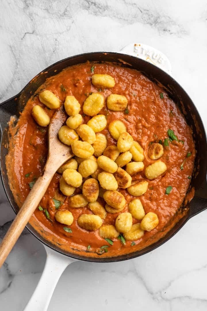 This one pot cheesy tomato gnocchi is creamy, comforting, and ready in under 30 minutes for an easy vegan weeknight dinner! Stirring toasted gnocchi into skillet of creamy tomato sauce.