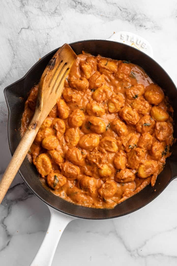 This one pot cheesy tomato gnocchi is creamy, comforting, and ready in under 30 minutes for an easy vegan weeknight dinner! Skillet of cheesy tomato gnocchi with slotted spoon.