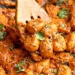 Wooden slotted spoon stirring cheesy tomato gnocchi.