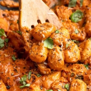 Wooden slotted spoon stirring cheesy tomato gnocchi.