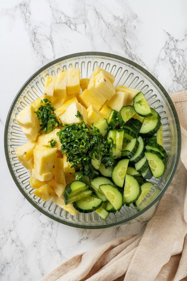 This easy pineapple cucumber salad is crisp, juicy and tossed in a tangy lime dressing. It’s refreshing, quick and perfect for summer! Cilantro, pineapple, and cucumber in mixing bowl.