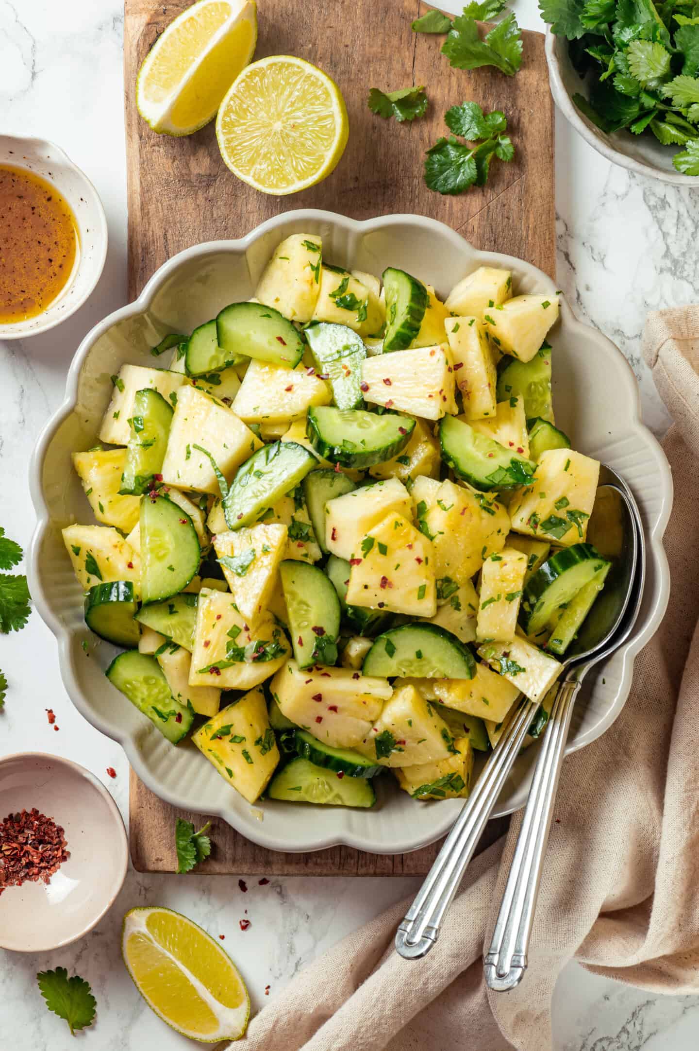 This easy pineapple cucumber salad is crisp, juicy and tossed in a tangy lime dressing. It’s refreshing, quick and perfect for summer! Bowl of pineapple cucumber salad on wooden board.