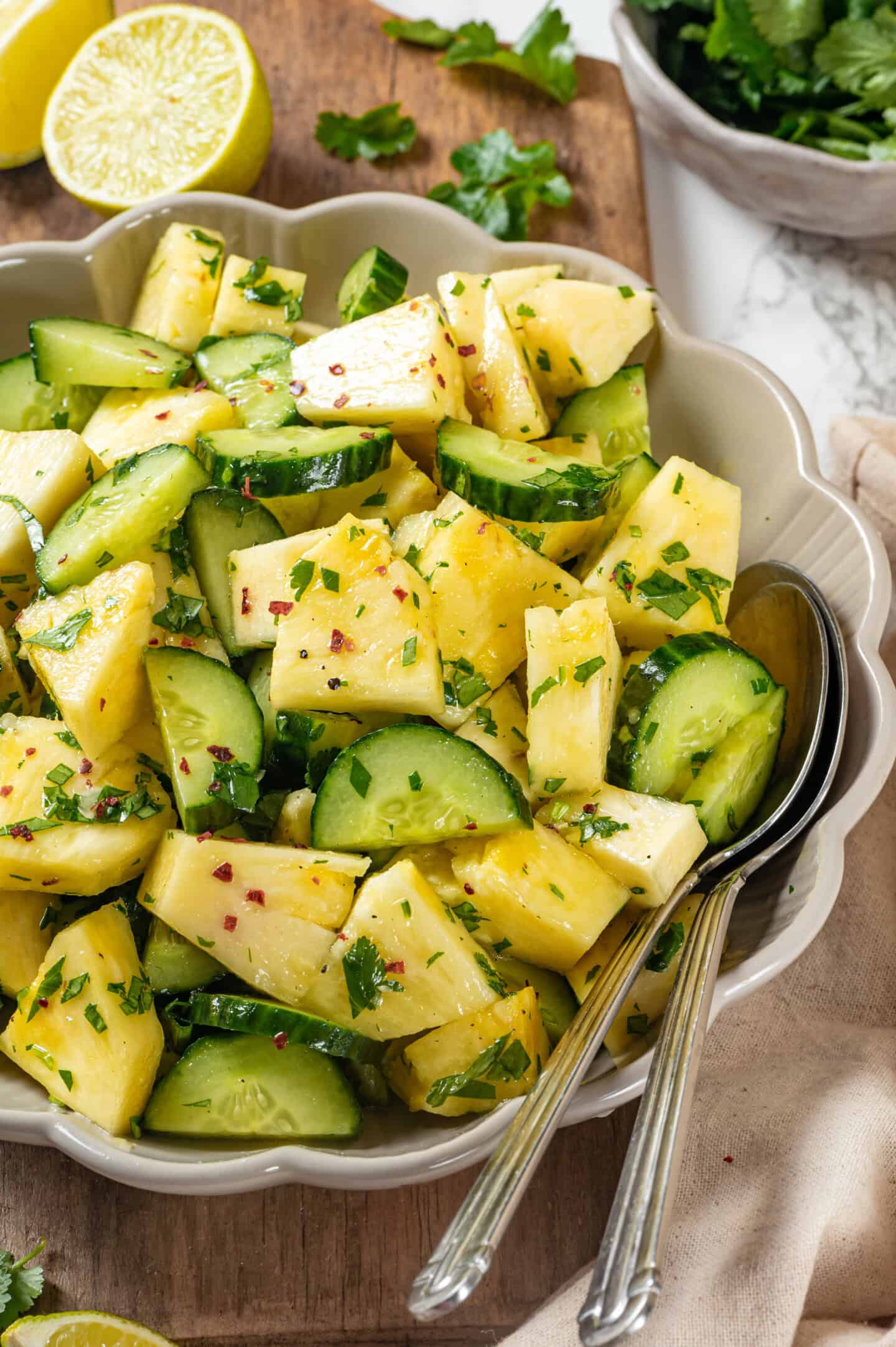This easy pineapple cucumber salad is crisp, juicy and tossed in a tangy lime dressing. It’s refreshing, quick and perfect for summer! Two spoons in bowl of pineapple cucumber salad.