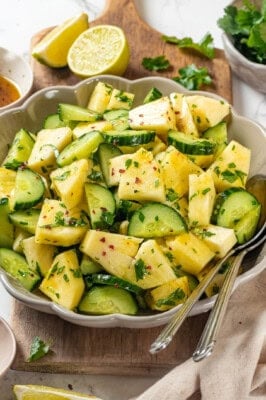 Pineapple cucumber salad in bowl with two spoons.
