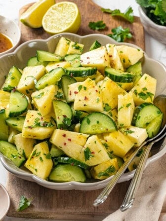 Pineapple cucumber salad in bowl with two spoons.