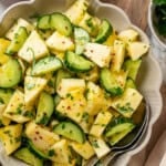 Pineapple cucumber salad in bowl with two spoons.