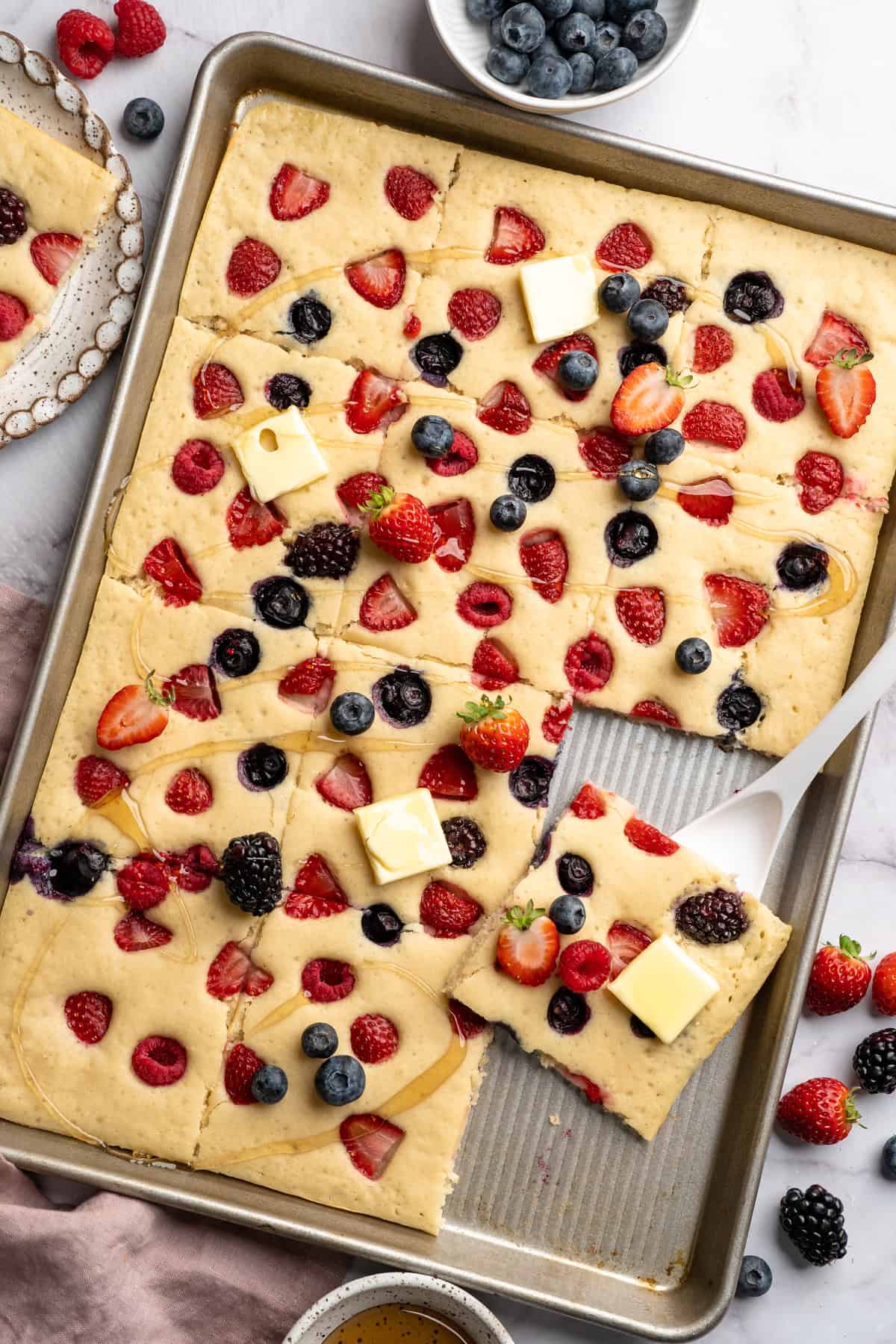 These fluffy sheet pan pancakes bake in one pan for an easy, no-flip breakfast that’s perfect for busy mornings or brunch. Pan of sliced sheet pan pancakes with berries.
