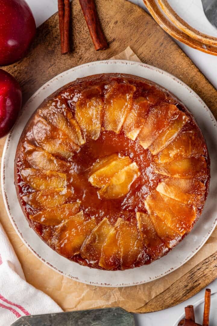 This easy upside down apple cake features tender, spiced cake topped with sticky caramel apples. It’s cozy, simple and perfect for fall! Whole upside down apple cake on plate.