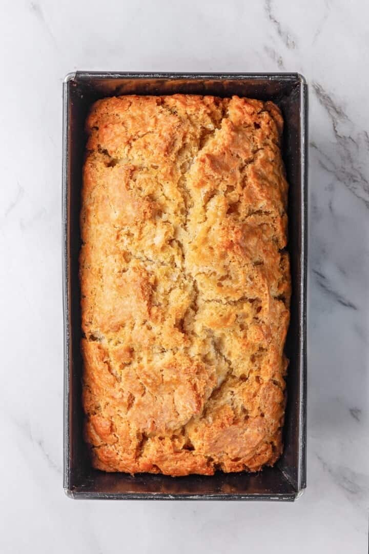 This easy beer bread recipe is soft, moist and baked with a crisp golden crust. It’s a simple no-knead loaf ready to eat in under an hour! Pan of beer bread with golden crust.