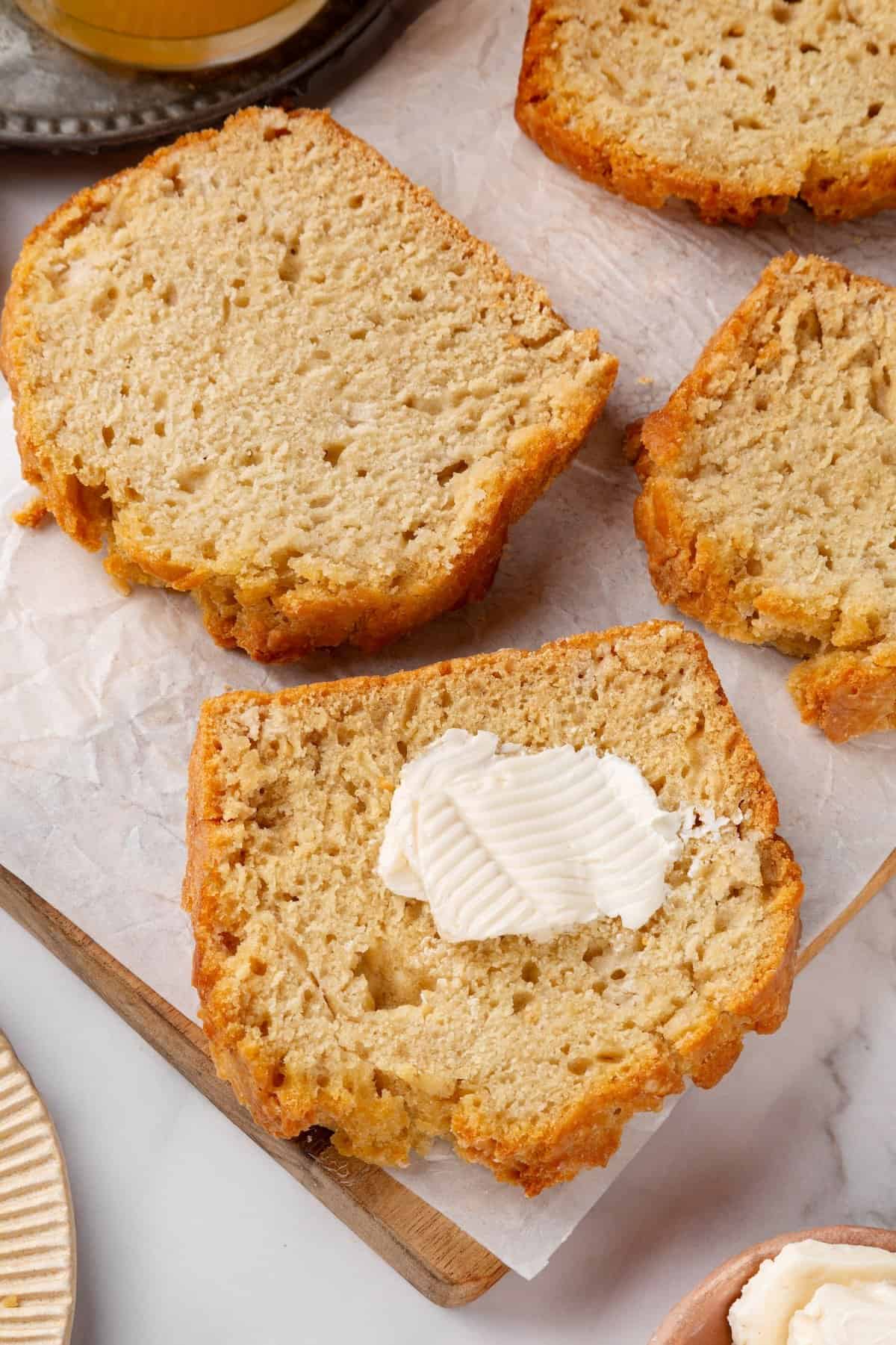 This easy beer bread recipe is soft, moist and baked with a crisp golden crust. It’s a simple no-knead loaf ready to eat in under an hour! Slices of beer bread, with one topped with vegan butter.