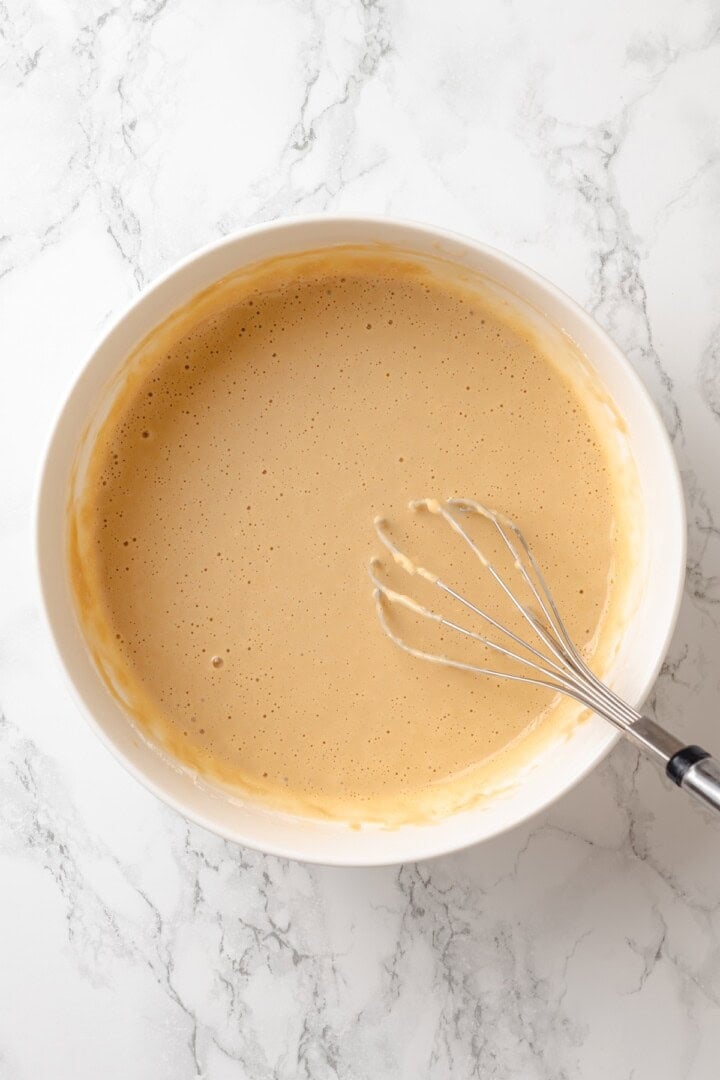 German pancakes bake up puffy and golden with crisp edges and a tender middle. Aquafaba stands in for the eggs in this easy vegan recipe! Batter for vegan German pancake in bowl with whisk.