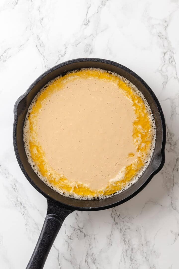 German pancakes bake up puffy and golden with crisp edges and a tender middle. Aquafaba stands in for the eggs in this easy vegan recipe! Vegan German pancake batter in cast iron skillet.