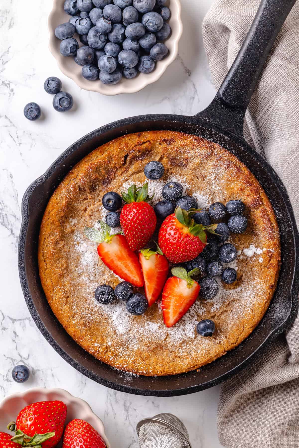German pancakes bake up puffy and golden with crisp edges and a tender middle. Aquafaba stands in for the eggs in this easy vegan recipe! German pancake in cast iron pancake topped with fresh berries.