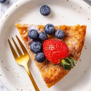 Slice of German panacke on plate with fork and fresh berries.