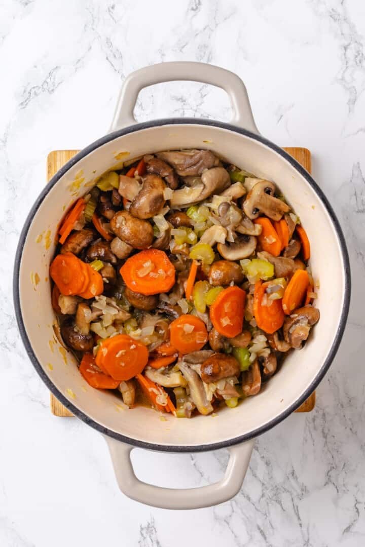 Mushroom bourguignon is a rich, savoury vegan stew simmered in red wine with herbs and meaty mushrooms. A cozy yet elegant meal! Mirepoix and mushrooms in Dutch oven.