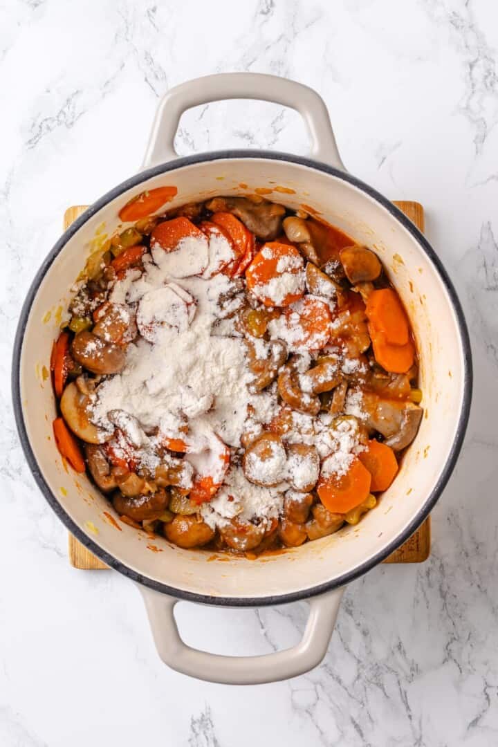 Mushroom bourguignon is a rich, savoury vegan stew simmered in red wine with herbs and meaty mushrooms. A cozy yet elegant meal! Flour added to pot for mushroom bourguignon.