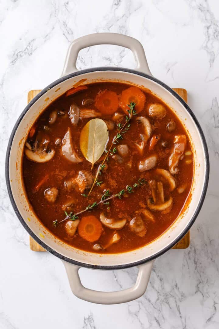 Mushroom bourguignon is a rich, savoury vegan stew simmered in red wine with herbs and meaty mushrooms. A cozy yet elegant meal! Thyme and bay leaf added to pot of mushroom bourguignon.
