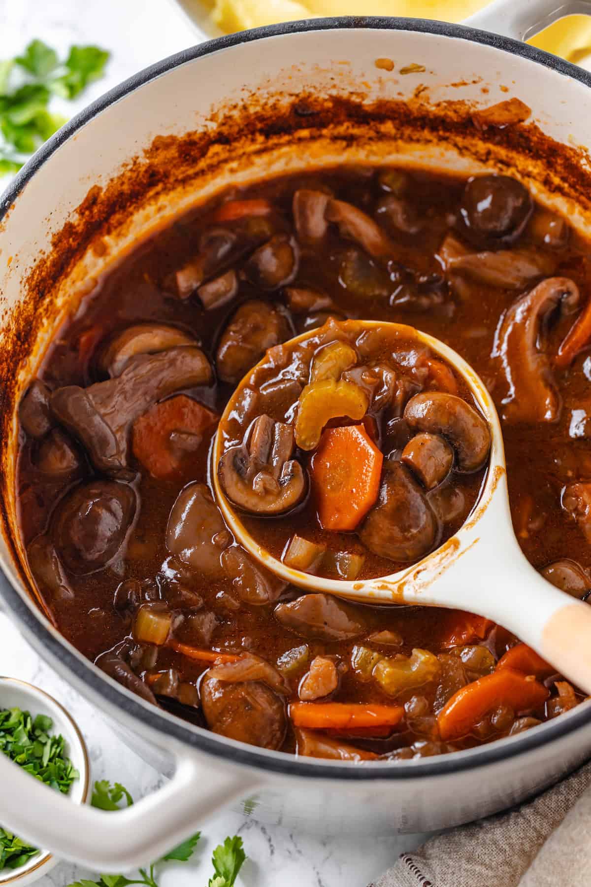 Mushroom bourguignon is a rich, savoury vegan stew simmered in red wine with herbs and meaty mushrooms. A cozy yet elegant meal! Ladle of mushroom bourguignon in pot.
