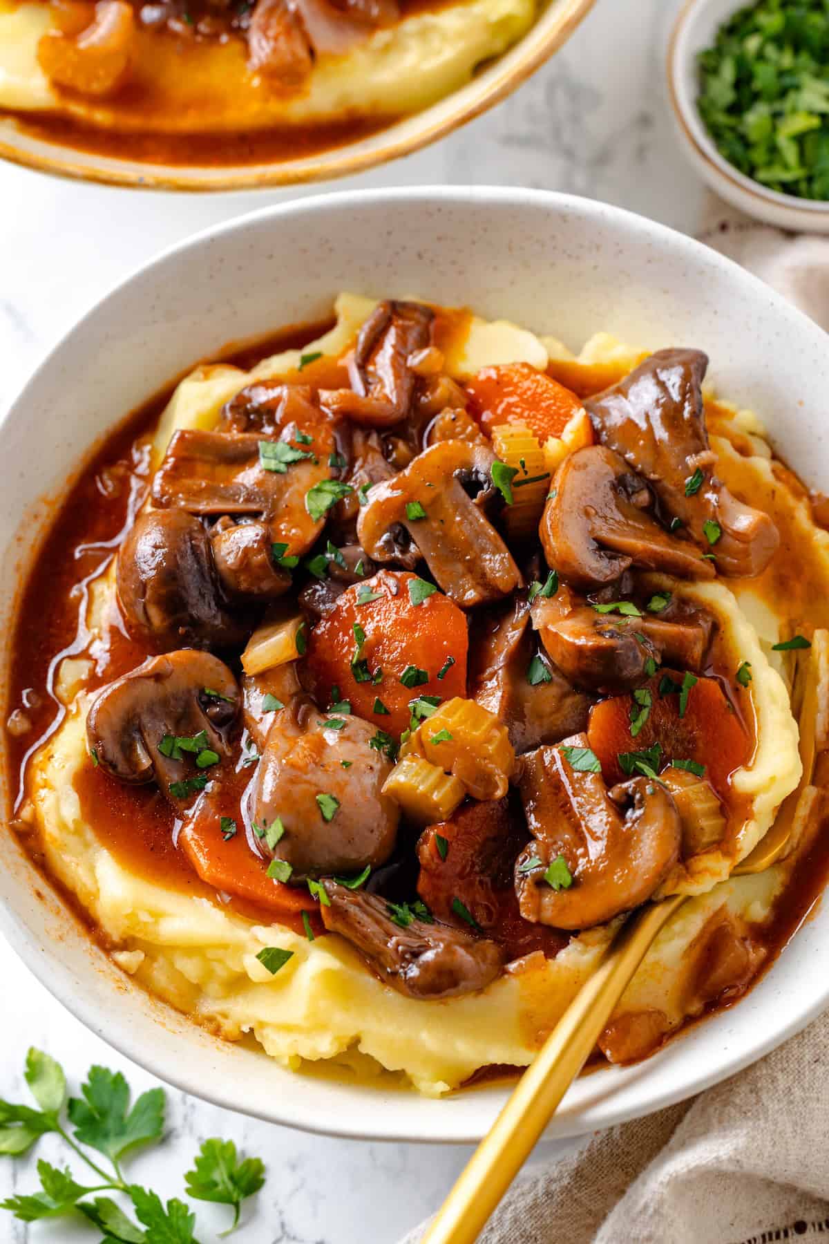 Mushroom bourguignon is a rich, savoury vegan stew simmered in red wine with herbs and meaty mushrooms. A cozy yet elegant meal! Bowl of mushroom bourguignon served over mashed potatoes.
